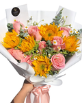 Bouquet of flowers with sunflowers and pink roses in white paper wrap, held by a hand.