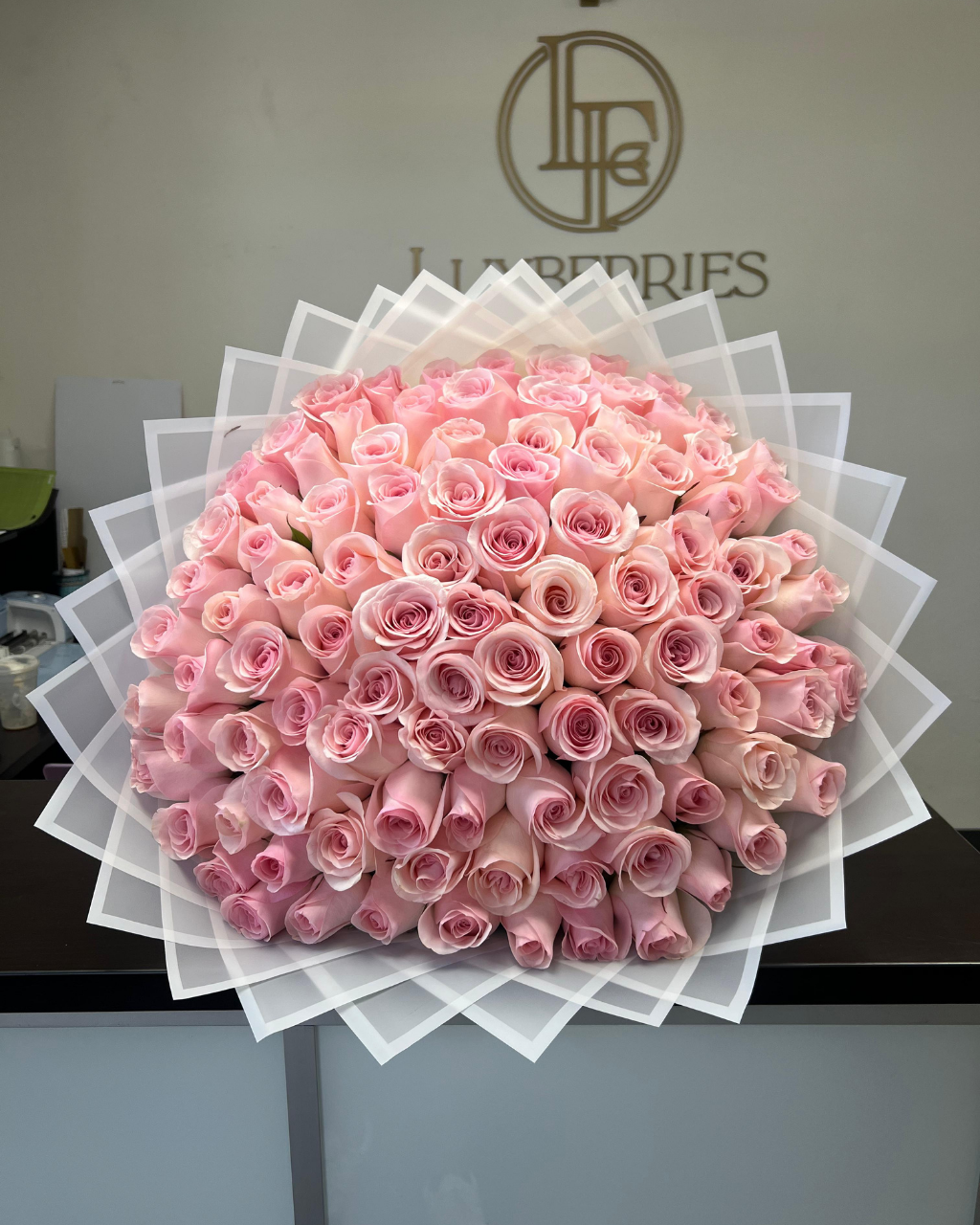 Bouquet of pink roses with a visible brand logo in the background