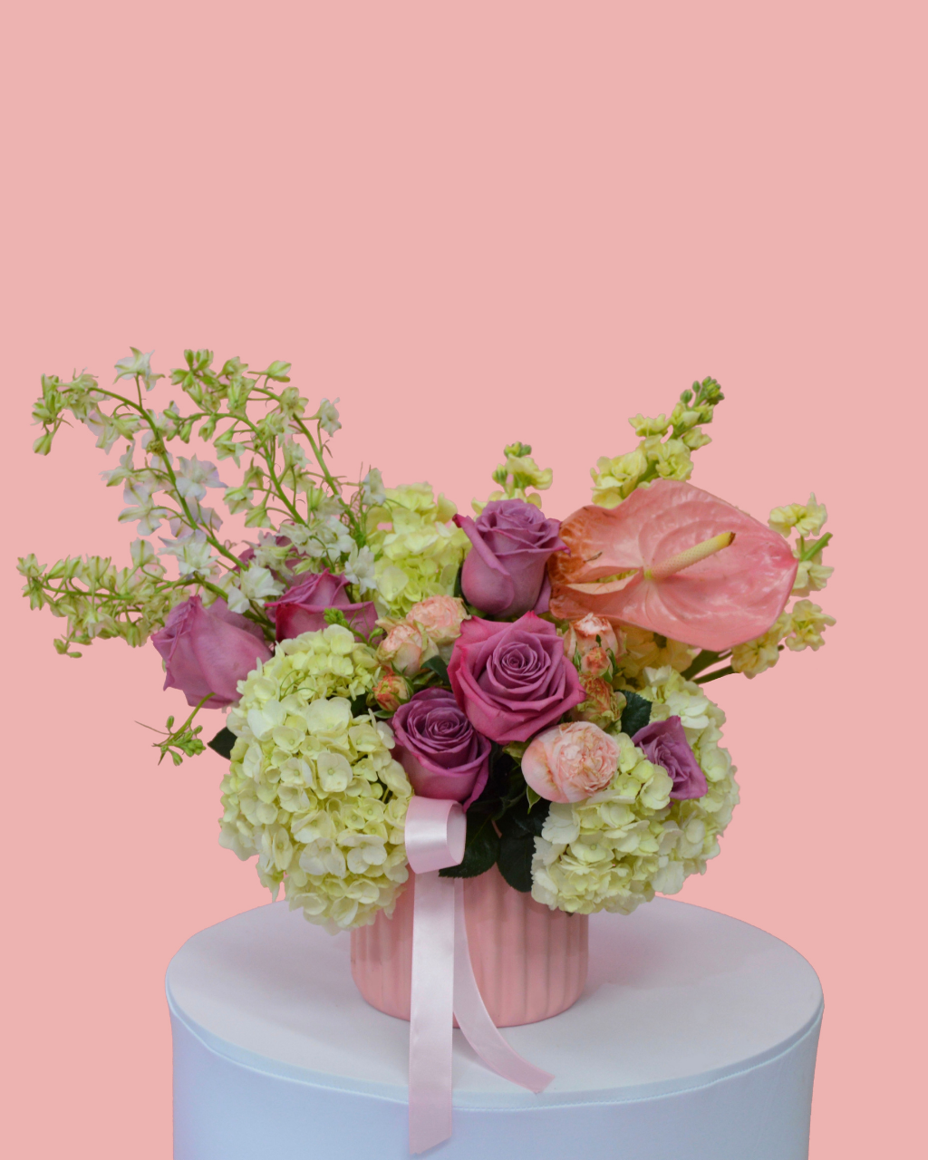 Floral arrangement with pink roses, hydrangeas, and anthuriums on a pink background