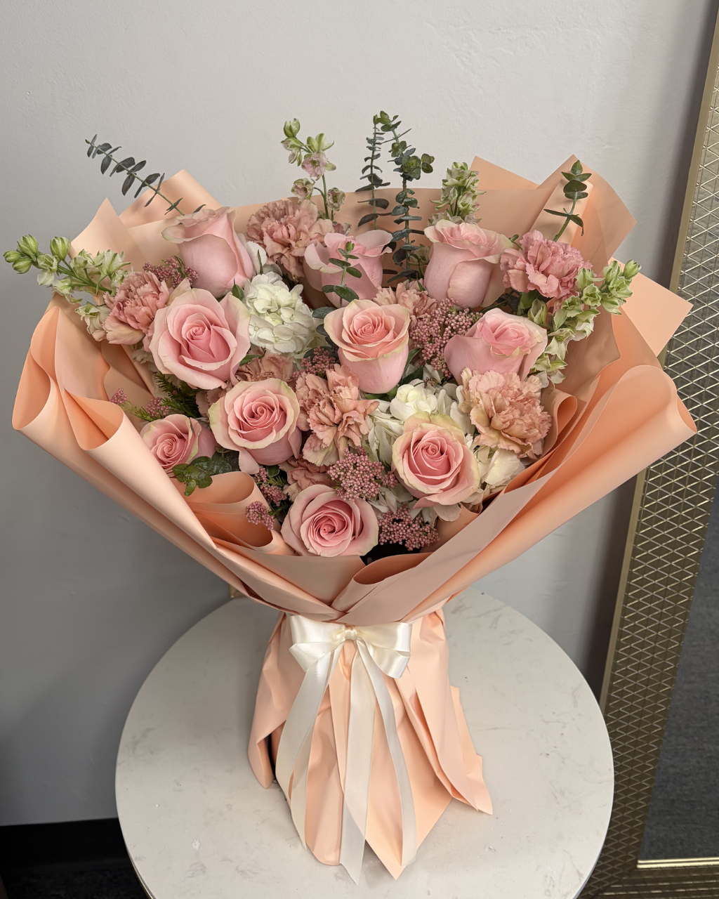 Bouquet of pink and white flowers wrapped in brown paper on a white surface.