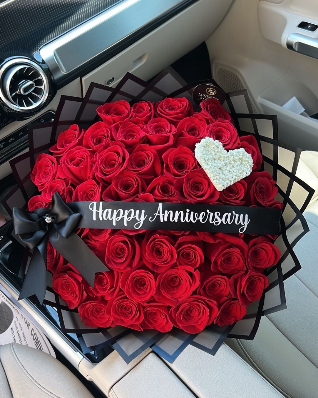 Heart-shaped arrangement of red roses with a 'Happy Anniversary' card inside a car.