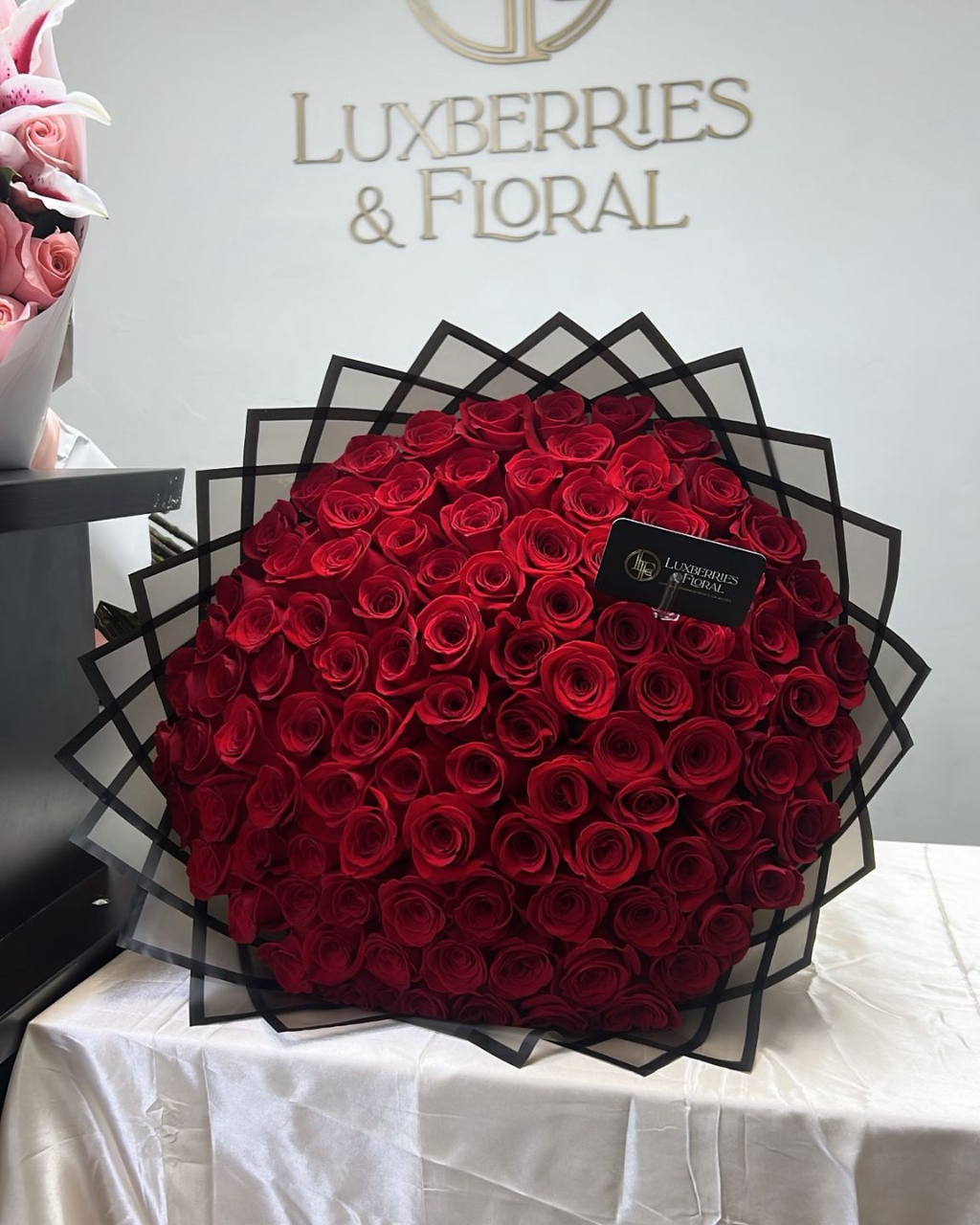Large bouquet of red roses in a black geometric container with Luxberries & Floral branding in the background.
