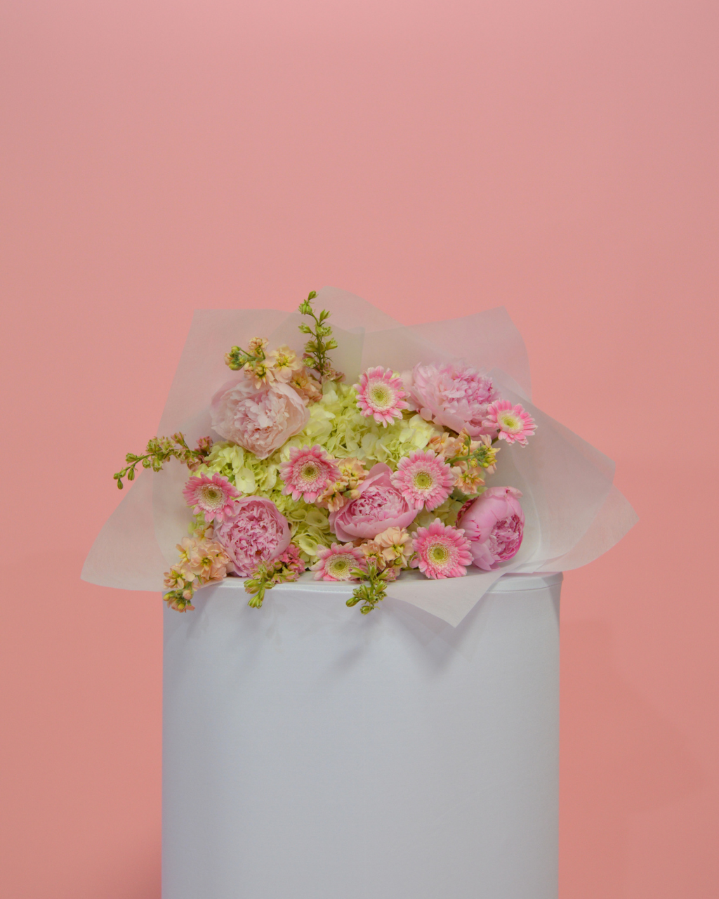 Bouquet of pink and green flowers wrapped in white paper with a pink ribbon on a white background