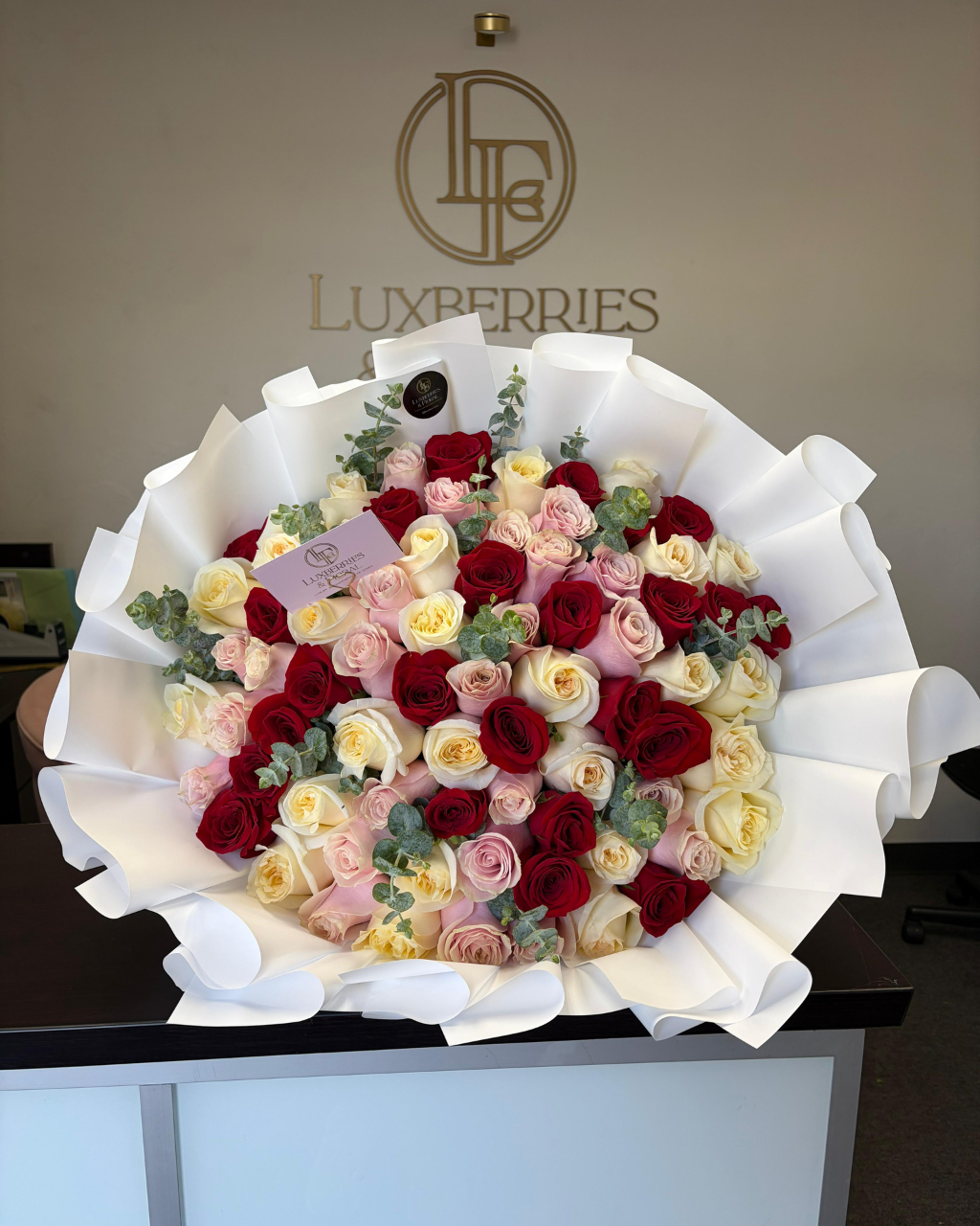 Bouquet of red, pink, and white roses with Luxberries logo in the background