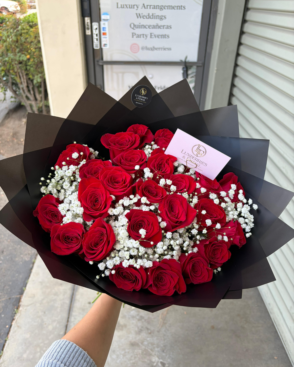 Bouquet of red roses with white berries in black paper wrapping, held by a person.