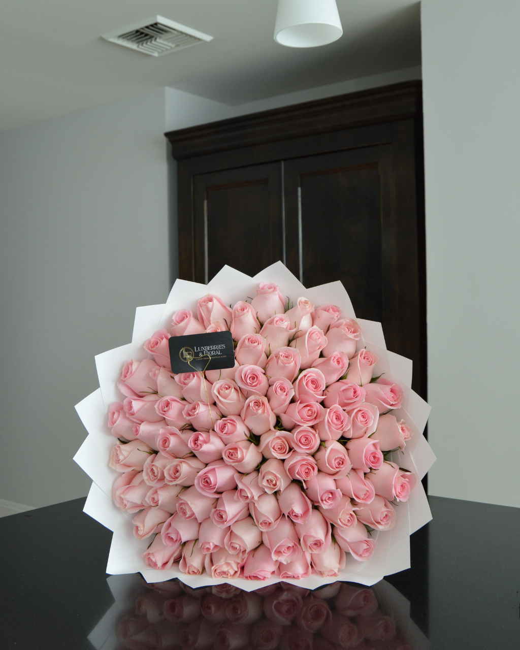 Bouquet of pink roses with a visible brand label on a reflective surface.
