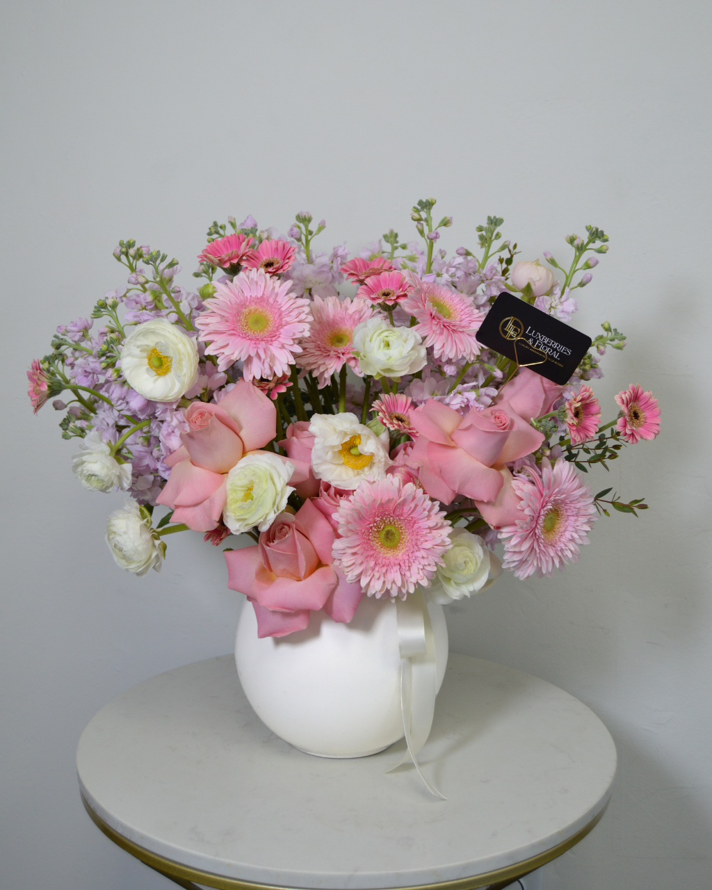 Bouquet of pink and white flowers in a white vase on a round table with a light gray background