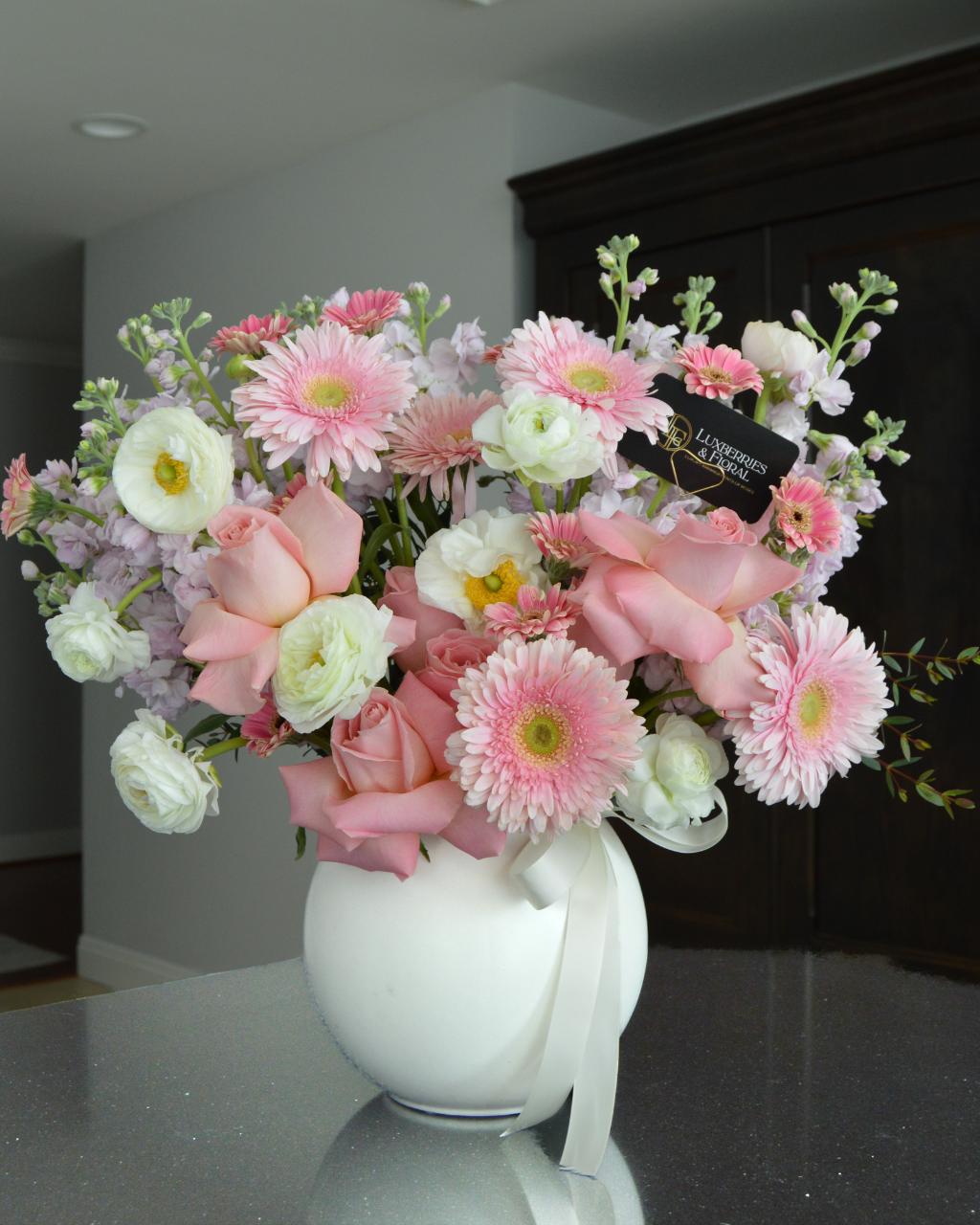 Bouquet of pink and white flowers in a white vase on a reflective surface.