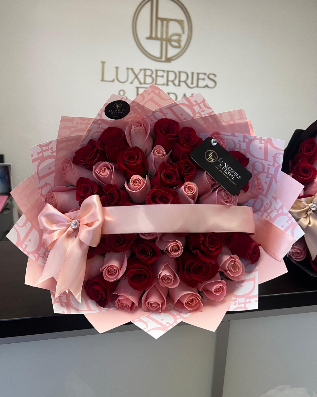 Bouquet of red and pink roses with a pink ribbon and 'Luxberries' logo in the background.