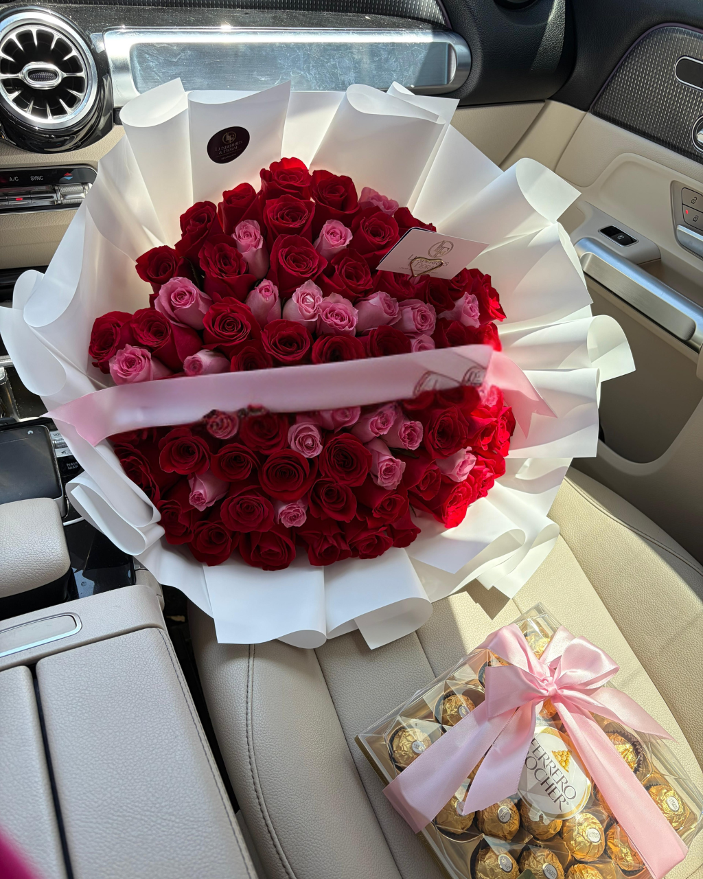 Bouquet of red and pink roses in a car with a box of chocolates.