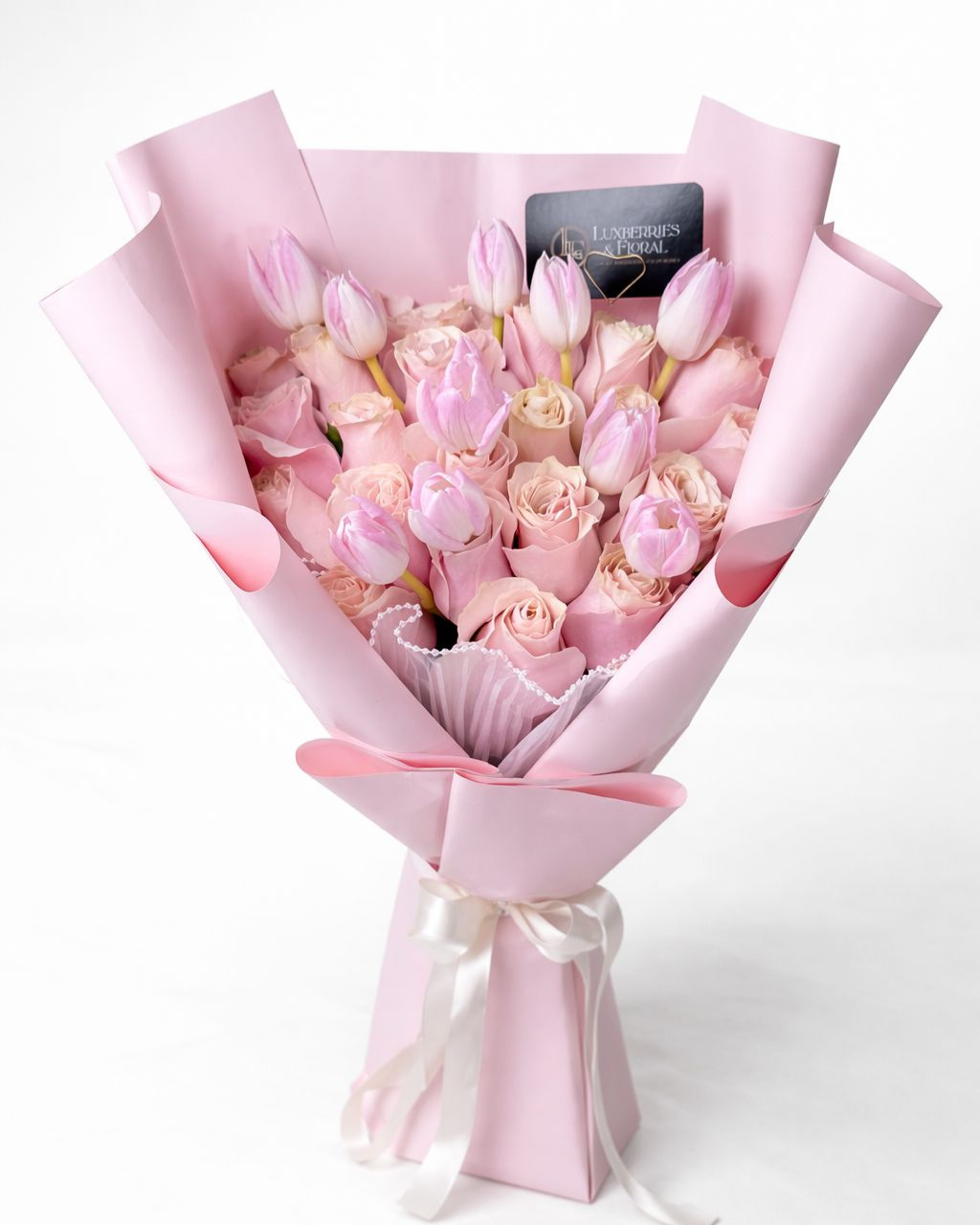 Bouquet of pink and white flowers wrapped in pink paper with a card on a white background