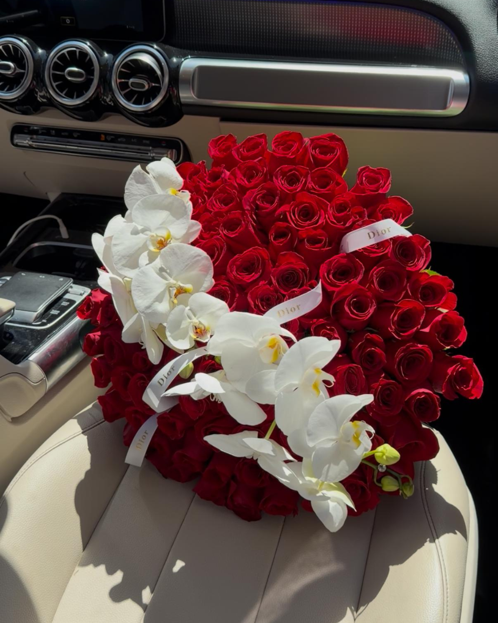 Heart-shaped arrangement of red roses and white orchids inside a car.