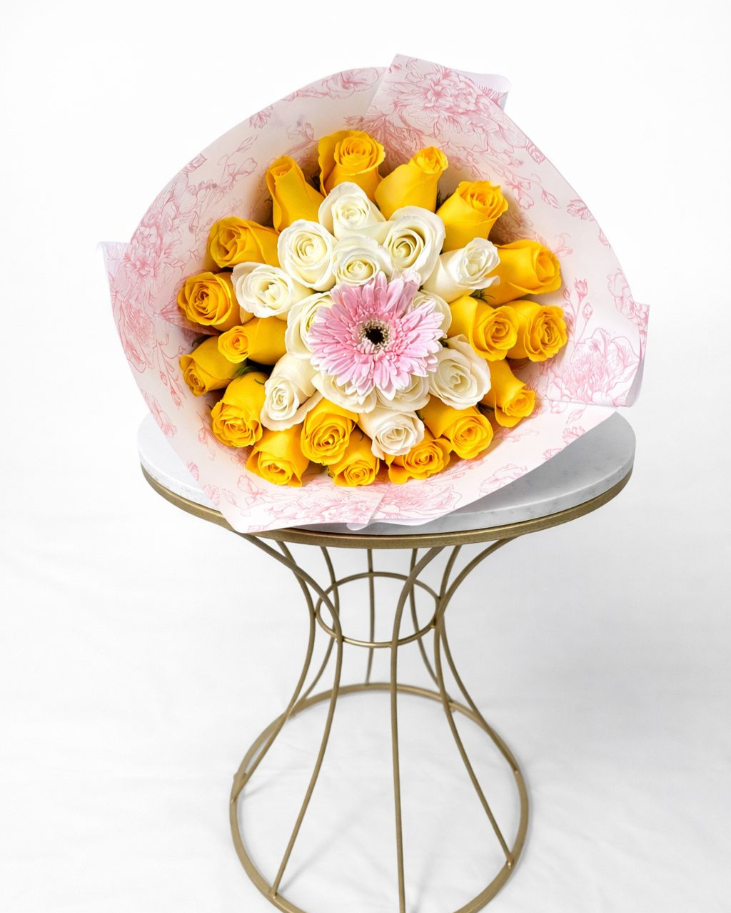 Bouquet of yellow and white flowers with a pink center on a small round table.