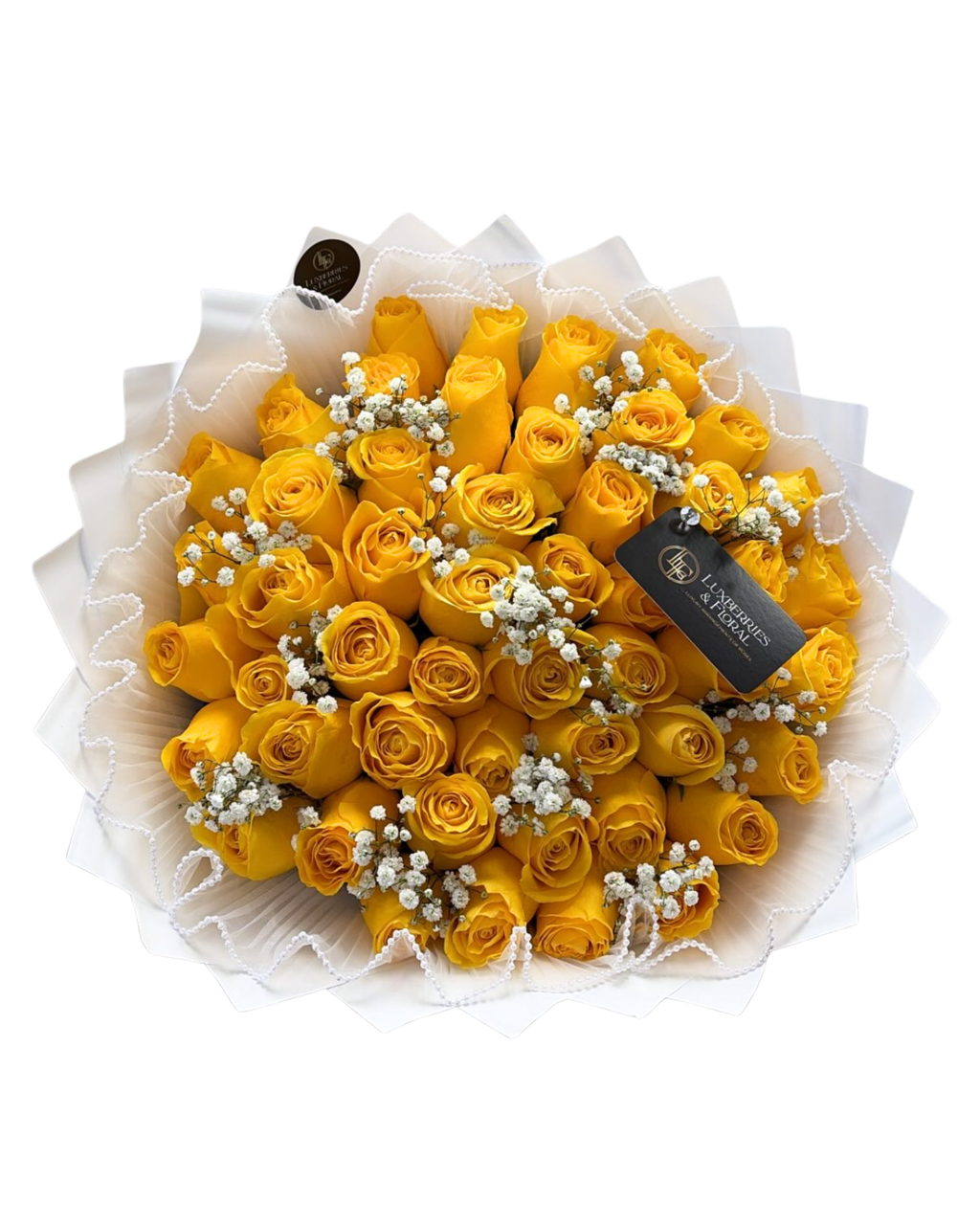A bouquet of yellow roses wrapped in white paper with small white filler flowers and a black gift tag, photographed on a plain white background.