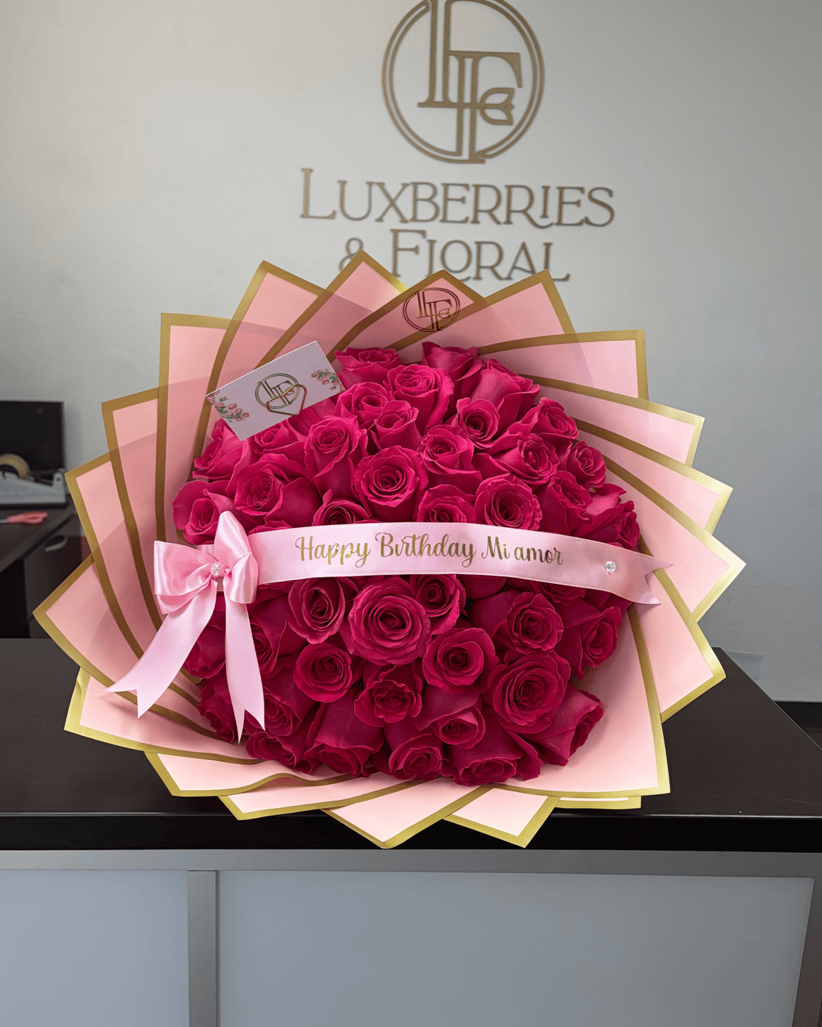 A large heart-shaped bouquet of magenta roses wrapped in pink paper,tied with a pink ribbon 'Happy Birthday, My love,'